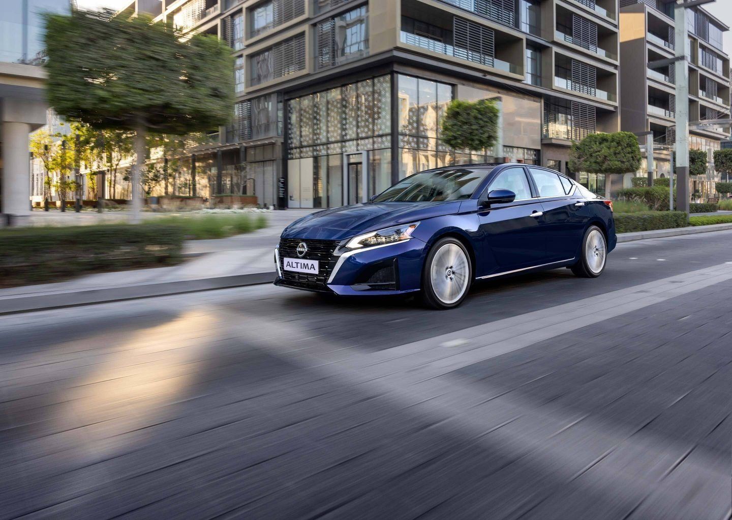 Blue Nissan Altima sedan driving through a modern urban district, highlighting its sleek exterior design and premium styling.