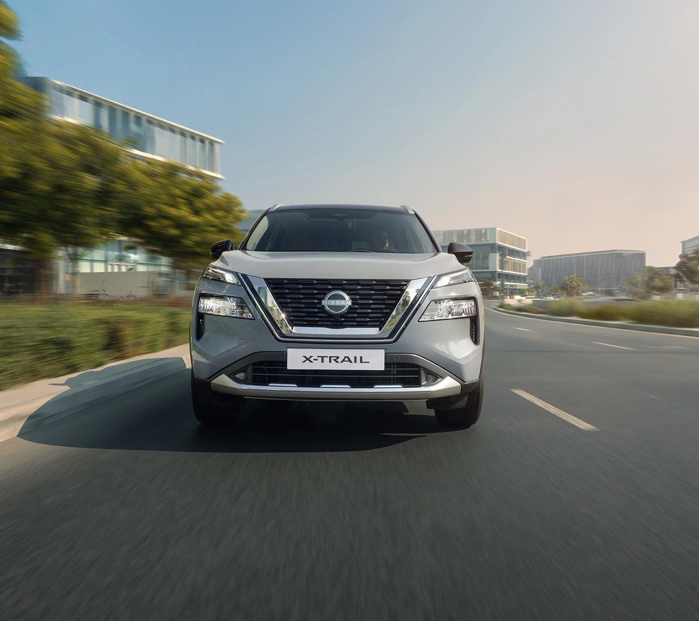 Front view of Nissan X-Trail SUV driving on a city road, featuring the signature V-Motion grille and modern LED headlights.