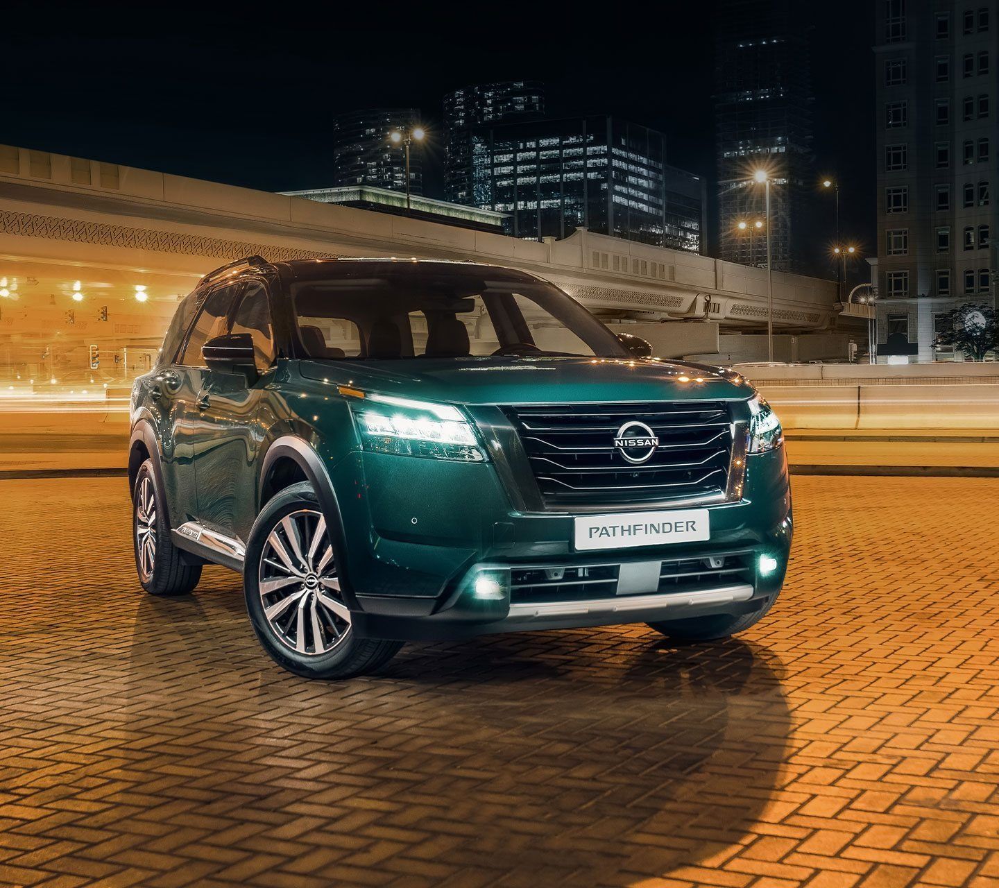 Green Nissan Pathfinder SUV parked in a cityscape at night, showcasing its premium exterior design and illuminated LED lighting.