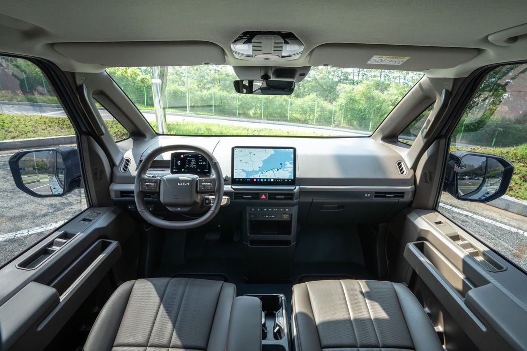 Wide front interior view of the Kia PV5 Passenger with minimalist dashboard, steering wheel and large central touchscreen.