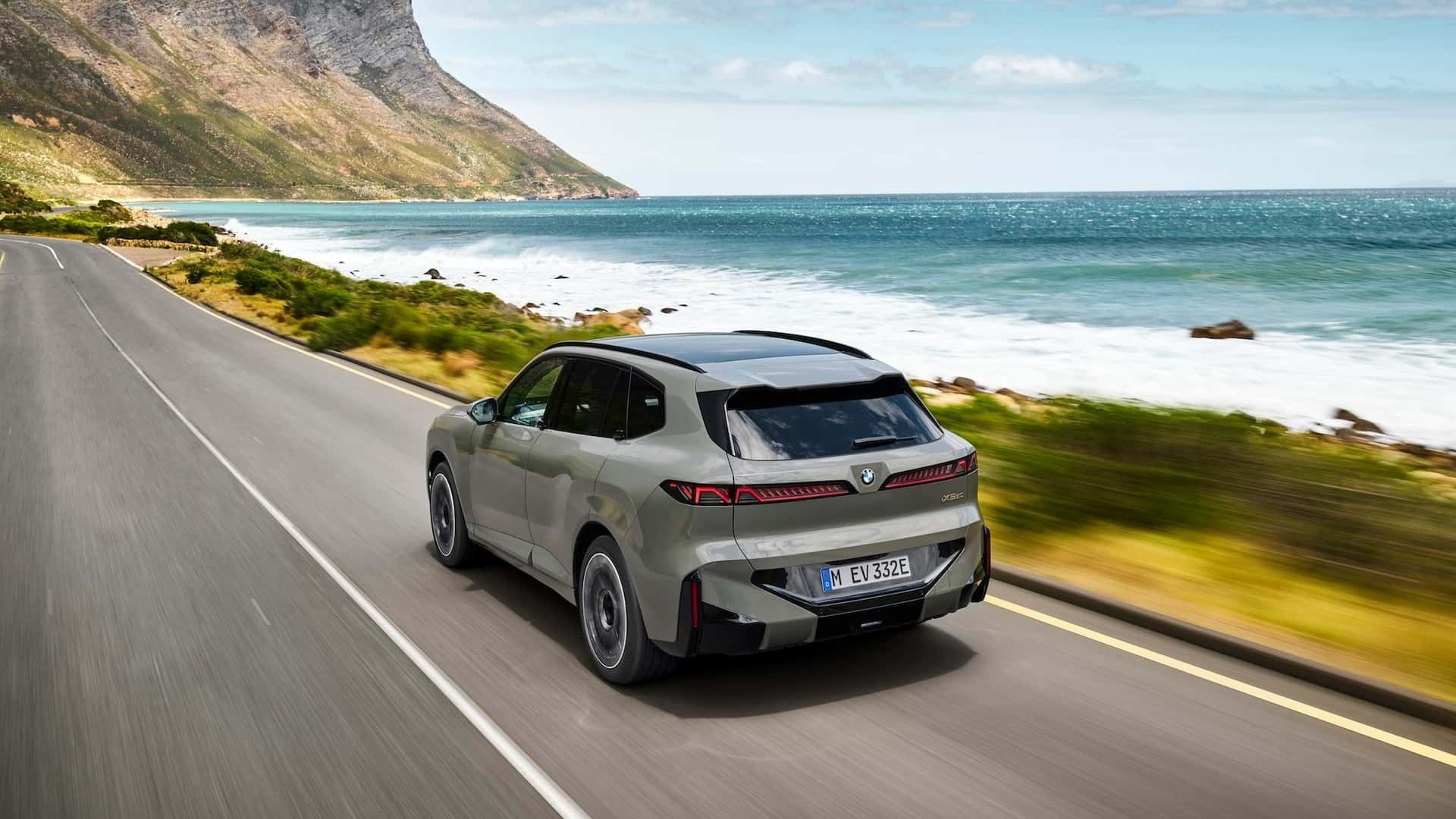 Rear three-quarter view of the BMW X5 driving along a coastal highway with redesigned LED taillights.