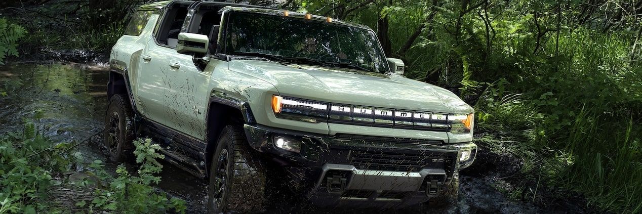 GMC Hummer EV pickup truck tackling a muddy off-road trail with rugged all-terrain capability