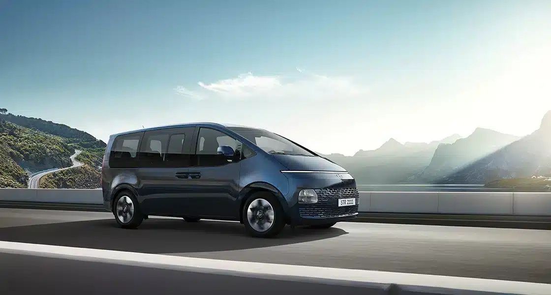 Hyundai STARIA driving on a scenic road with its futuristic MPV design on display.