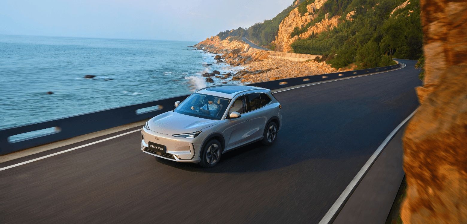 Geely EX5 electric SUV driving along a scenic coastal road with a panoramic sunroof.